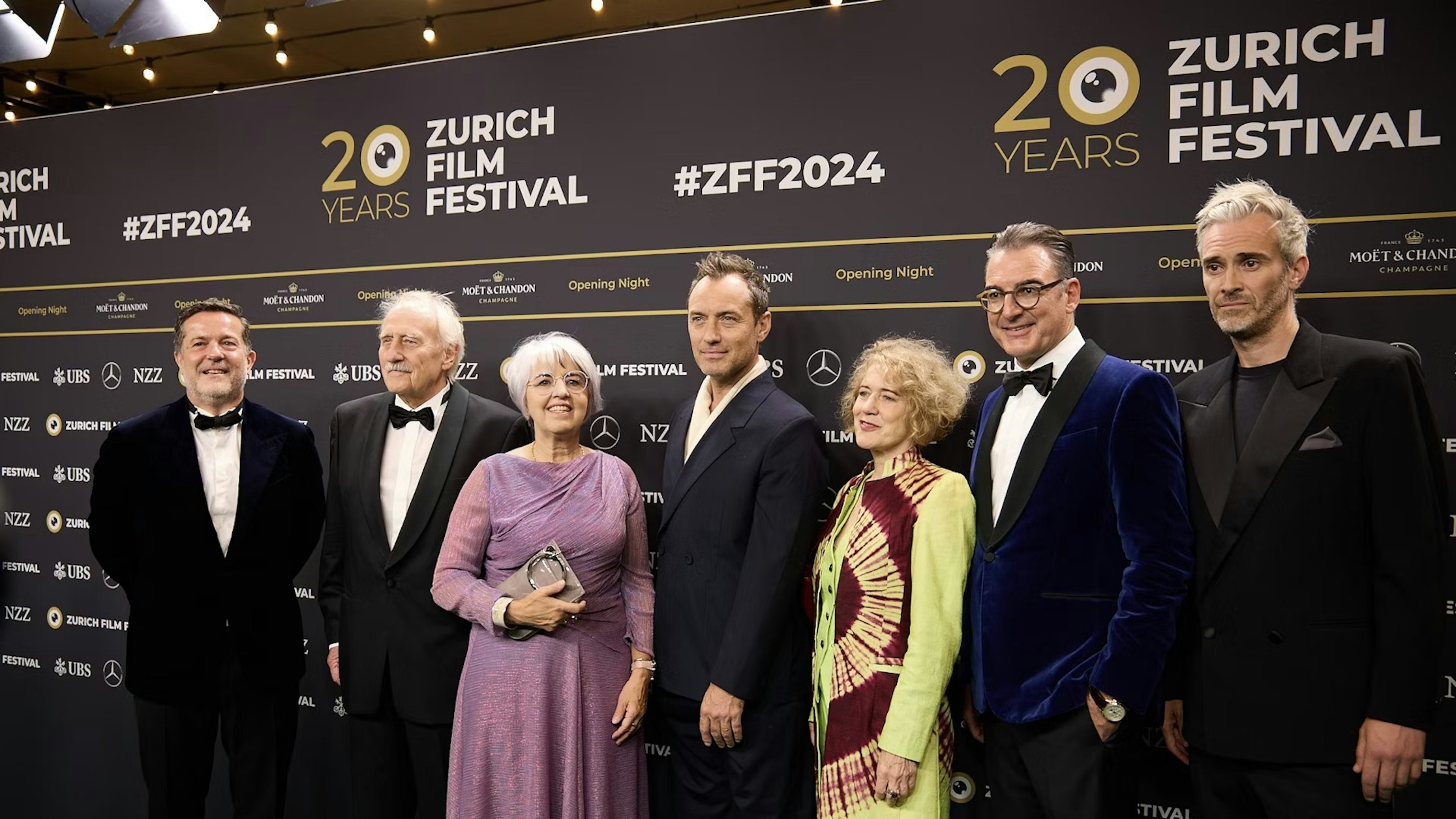 Eine Gruppe von sieben Personen in Abendgarderobe posiert gemeinsam auf dem roten Teppich des Zurich Film Festival vor einem Hintergrund mit dem Logo des Festivals und dem Text zum 20-jährigen Jubiläum.