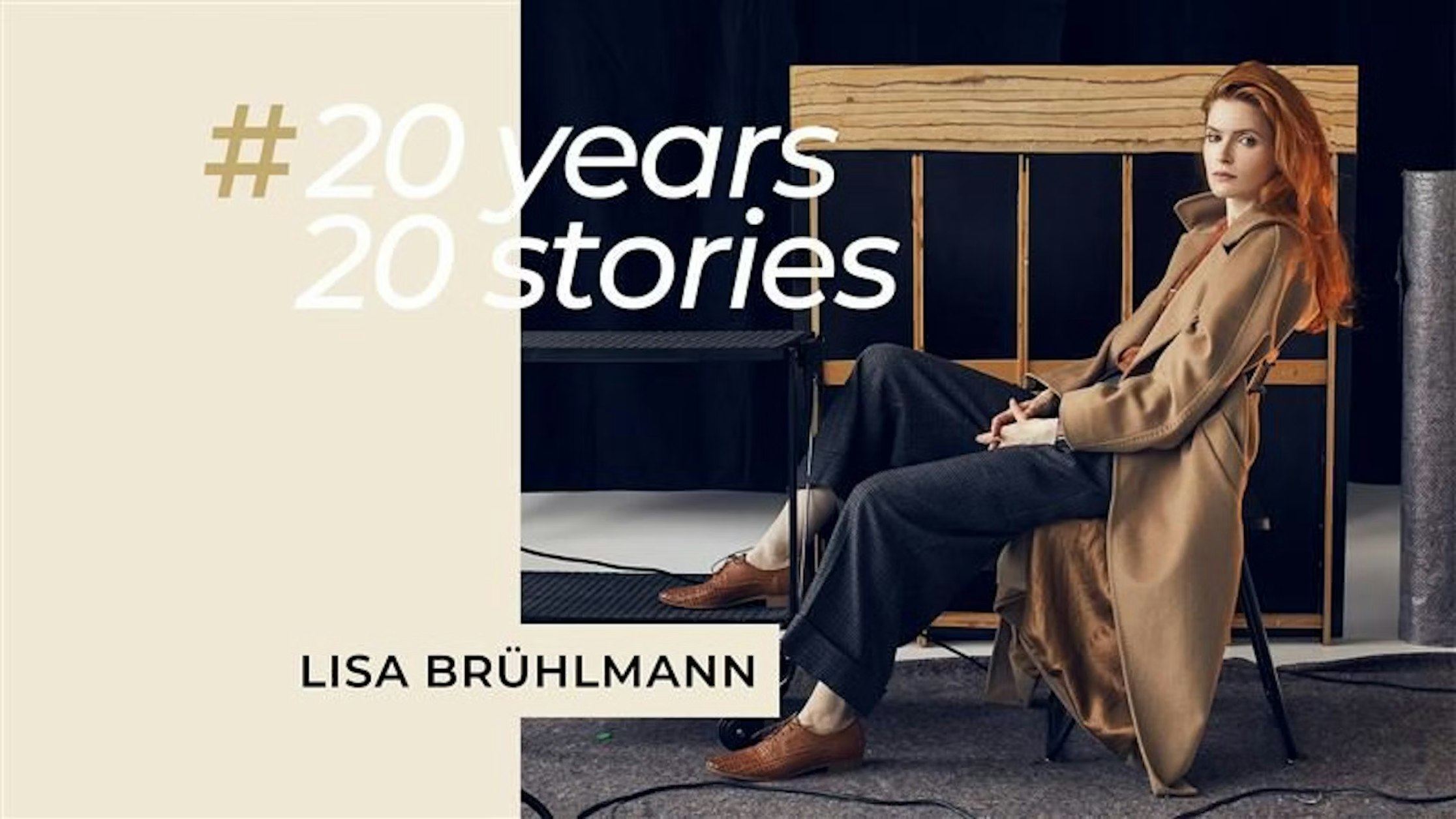 Eine Frau mit langen roten Haaren sitzt auf einem Stuhl und trägt einen hellbraunen Mantel und braune Schuhe. Der Text lautet: #20 Jahre, 20 Geschichten und Lisa Brühlmann. Sie steht neben einer Holzkonstruktion vor einem schlichten Hintergrund.