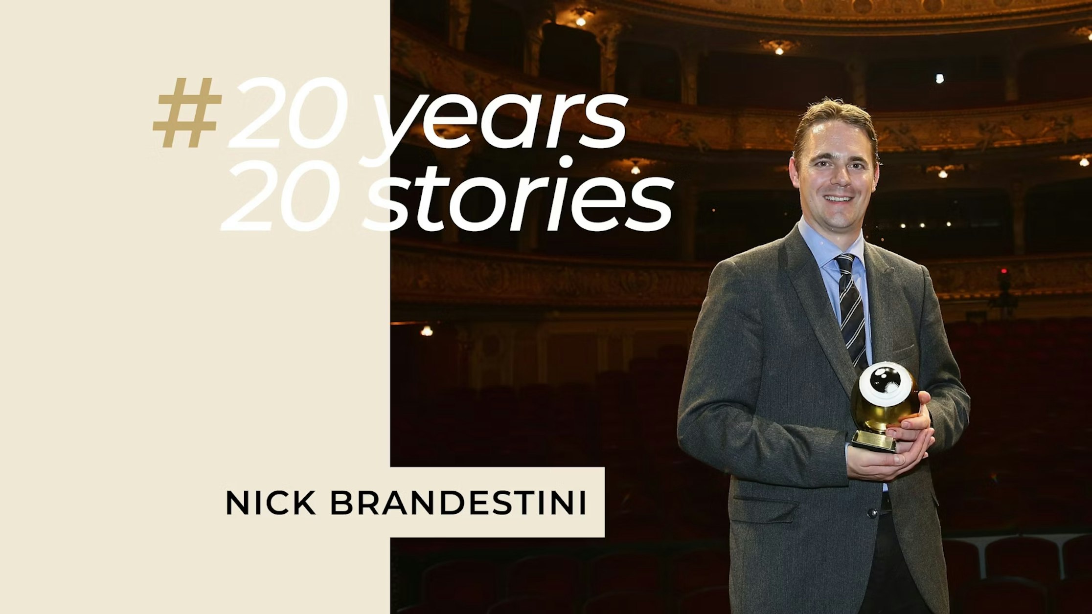 Ein lächelnder Mann im Anzug hält eine goldene Trophäe in einem Theater. Der Text lautet „#20 Jahre, 20 Geschichten“ und „Nick Brandestini“. Im Hintergrund sind verzierte Balkone und rote Sitze zu sehen.