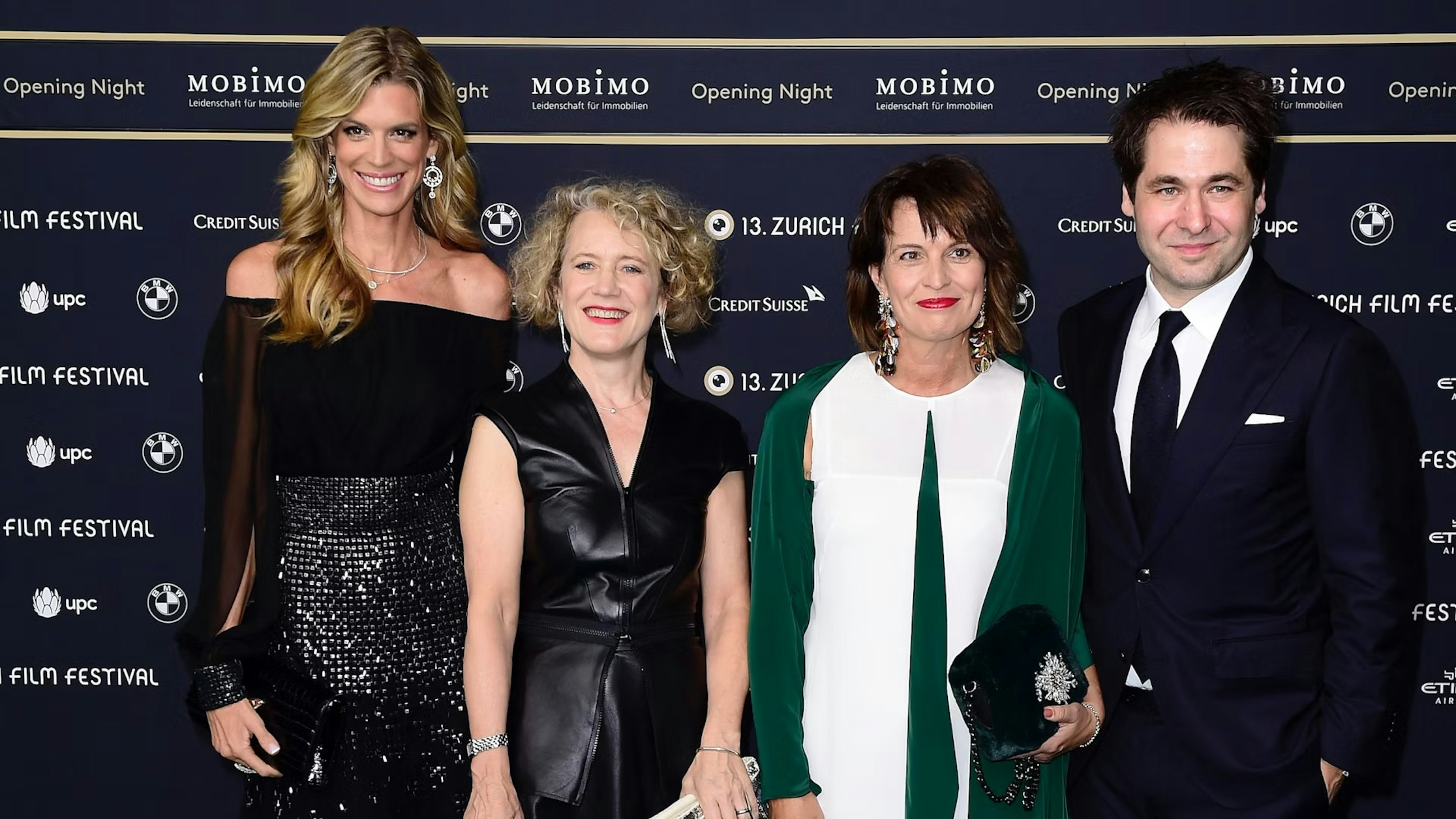 Vier formell gekleidete Personen stehen zusammen und lächeln auf einem roten Teppich beim Zurich Film Festival in die Kamera. Im Hintergrund sind die Logos der Veranstaltungssponsoren zu sehen.