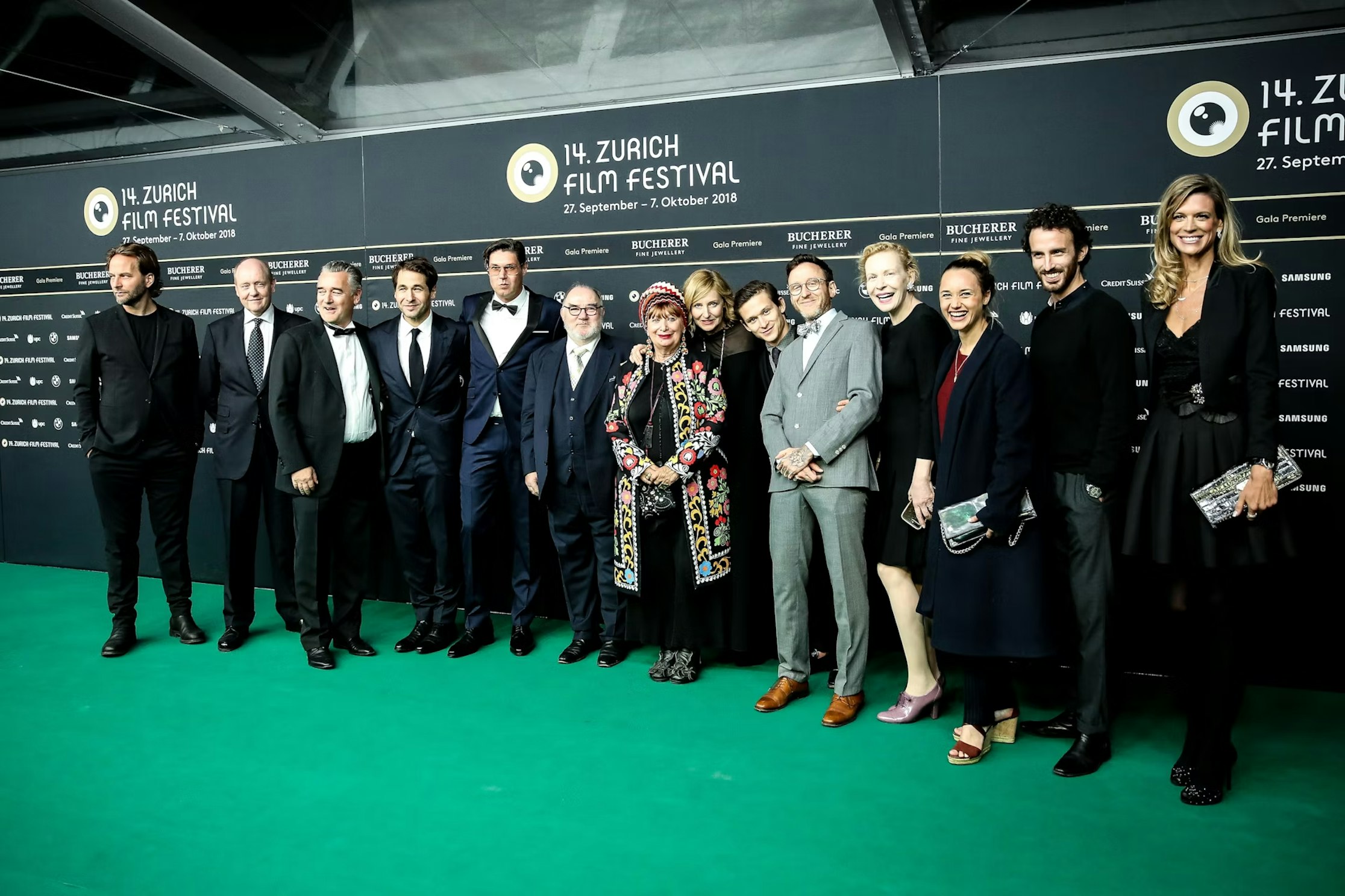 Eine Gruppe von Menschen in Abendgarderobe posiert gemeinsam auf einem grünen Teppich beim 14. Zurich Film Festival vor einem schwarzen Hintergrund mit Festivallogos und -texten.