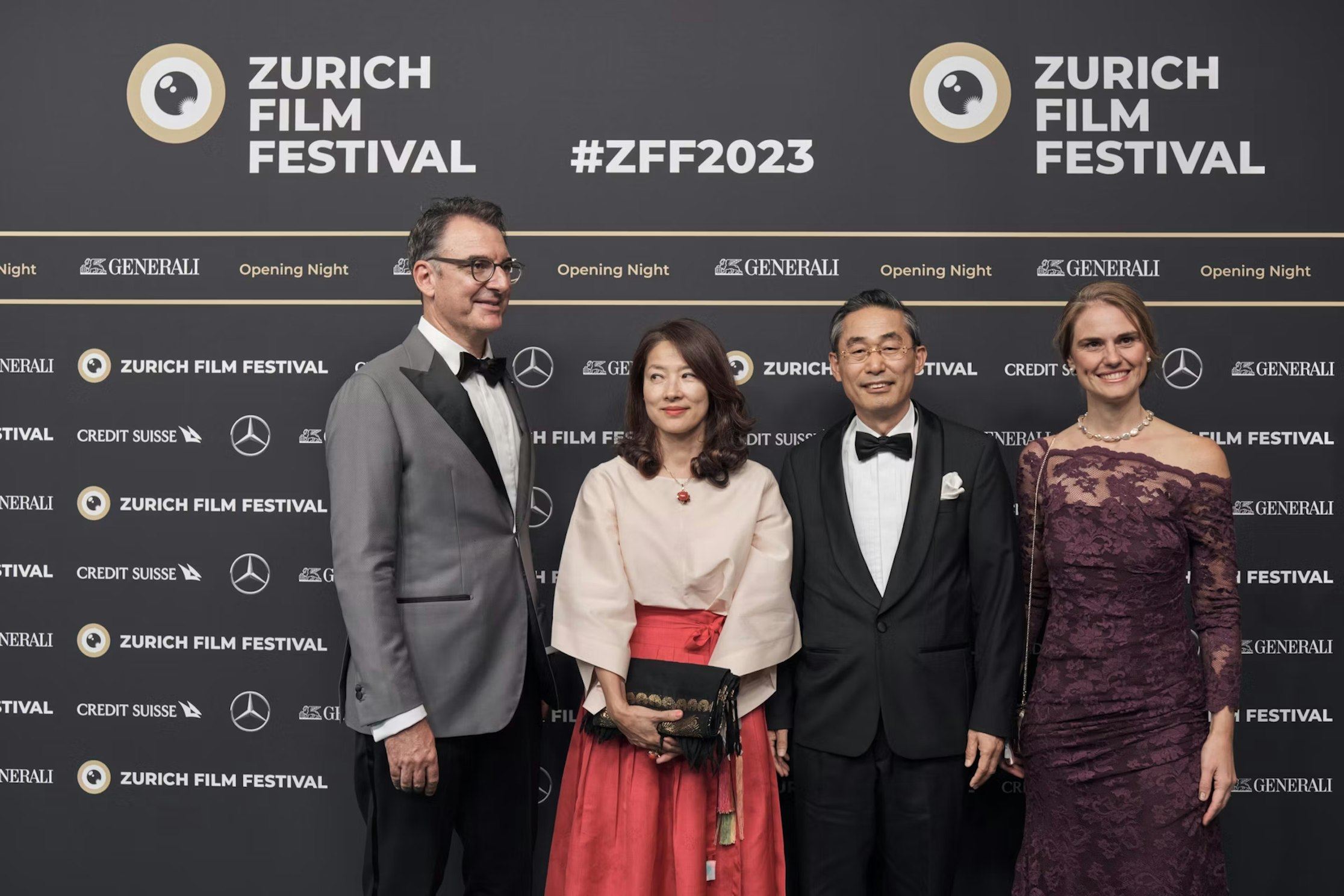 Vier Personen in Abendgarderobe posieren gemeinsam auf dem roten Teppich des Zurich Film Festival 2023, vor einer Kulisse mit Eventlogos und Sponsoren.