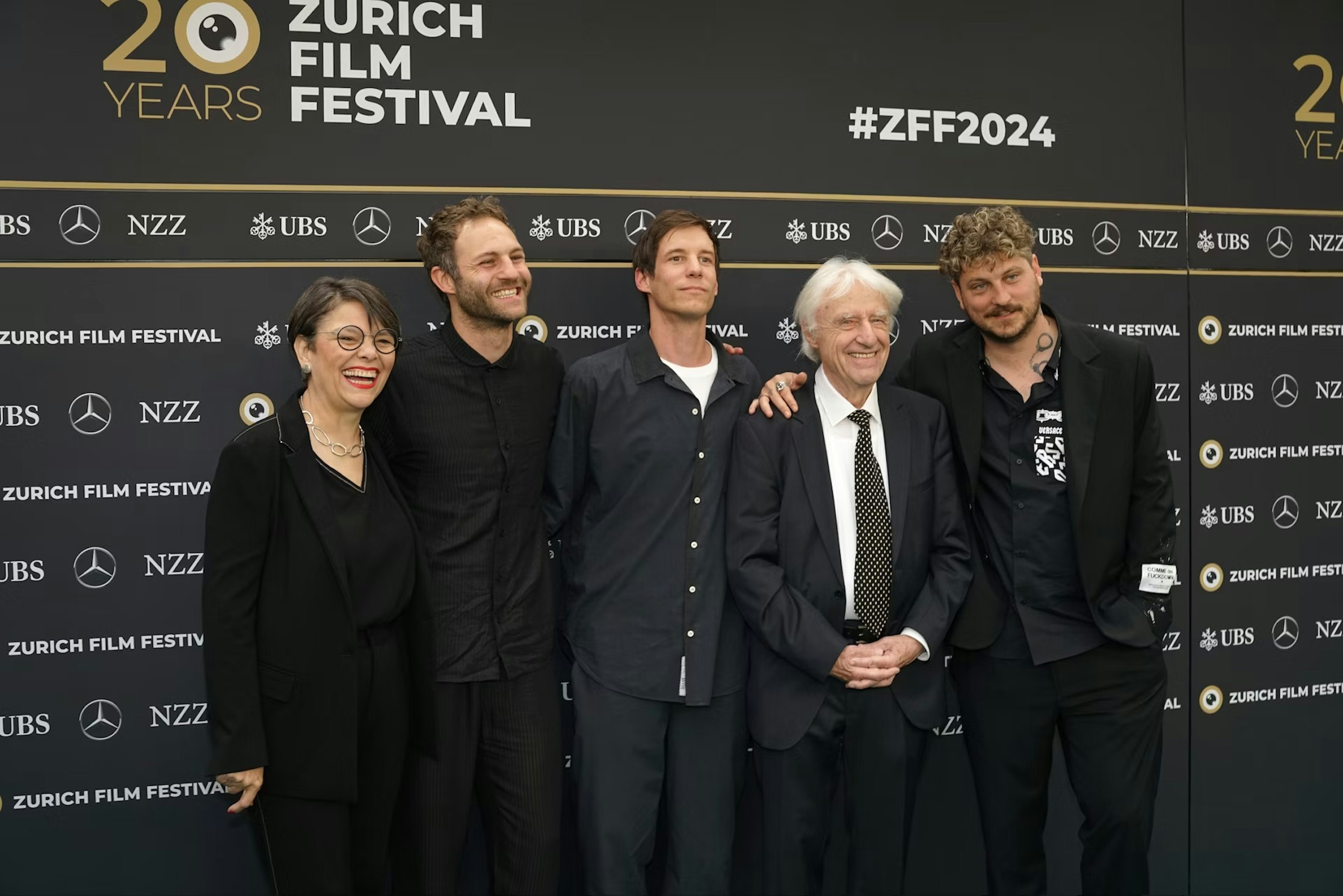 Fünf Menschen stehen und lächeln gemeinsam auf dem roten Teppich des Zurich Film Festival. Im Hintergrund befindet sich eine Kulisse mit Festival-Logos und dem Text „20 Jahre Zurich Film Festival #ZFF2024“.