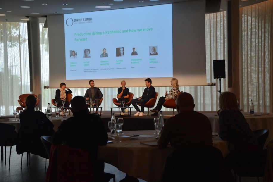 Auf der Bühne des Zurich Summit spricht ein sechsköpfiges Gremium über die Produktion während einer Pandemie und wie wir vorankommen, während das Publikum an runden Tischen in einem schwach beleuchteten Raum sitzt.