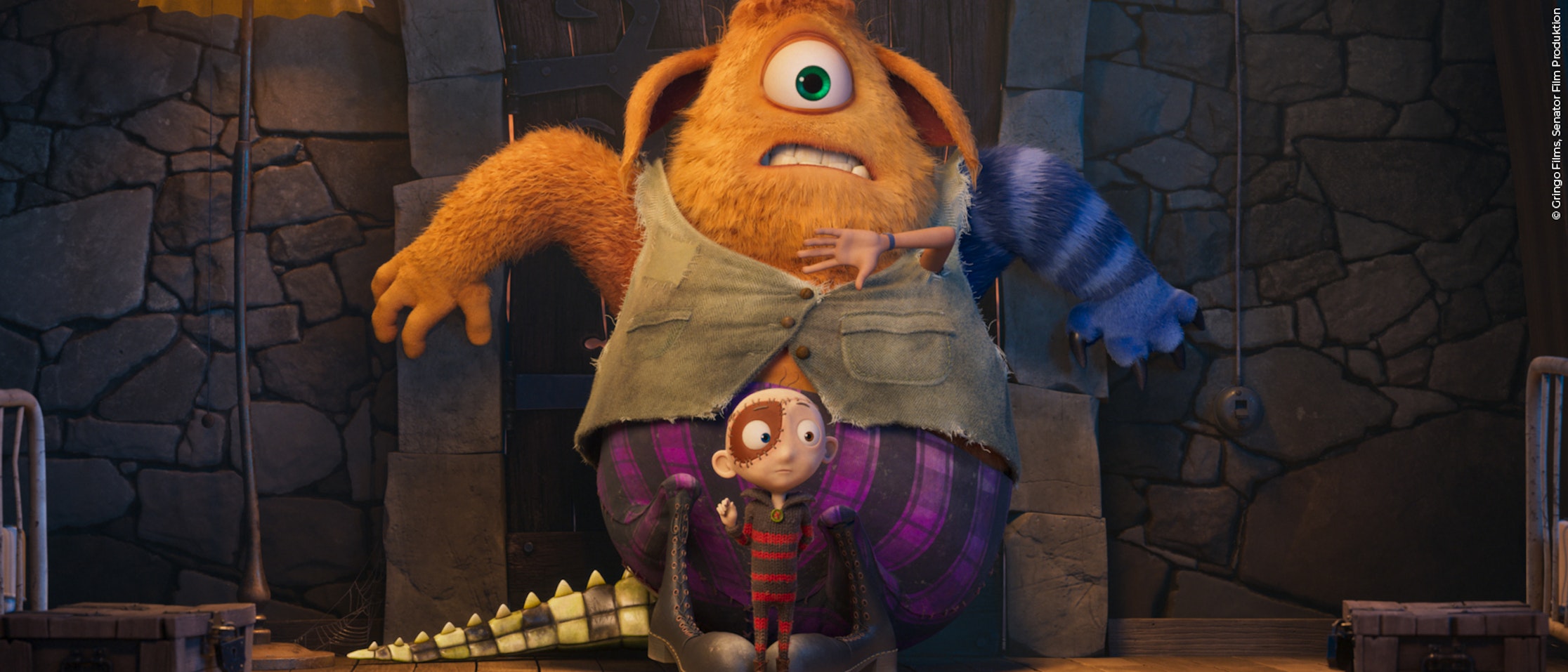 Ein großes, orangefarbenes, einäugiges Monster mit blau gestreiften Armen steht hinter einem kleinen, besorgten Kind mit blasser Haut und großen Augen in einem Raum mit Steinwänden. Das Monster trägt eine grüne Weste und eine lila Hose; ein Schwanz liegt auf dem Boden.