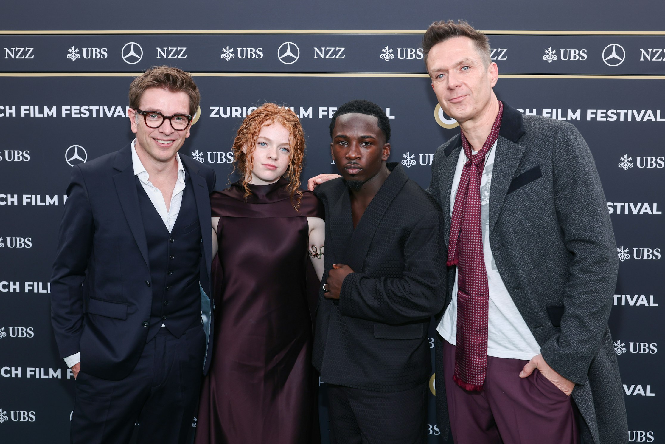 Vier Personen posieren gemeinsam auf dem roten Teppich des Zurich Film Festival vor einer Kulisse mit Logos wie UBS, NZZ und Mercedes-Benz. Sie sind formell und stilvoll gekleidet.