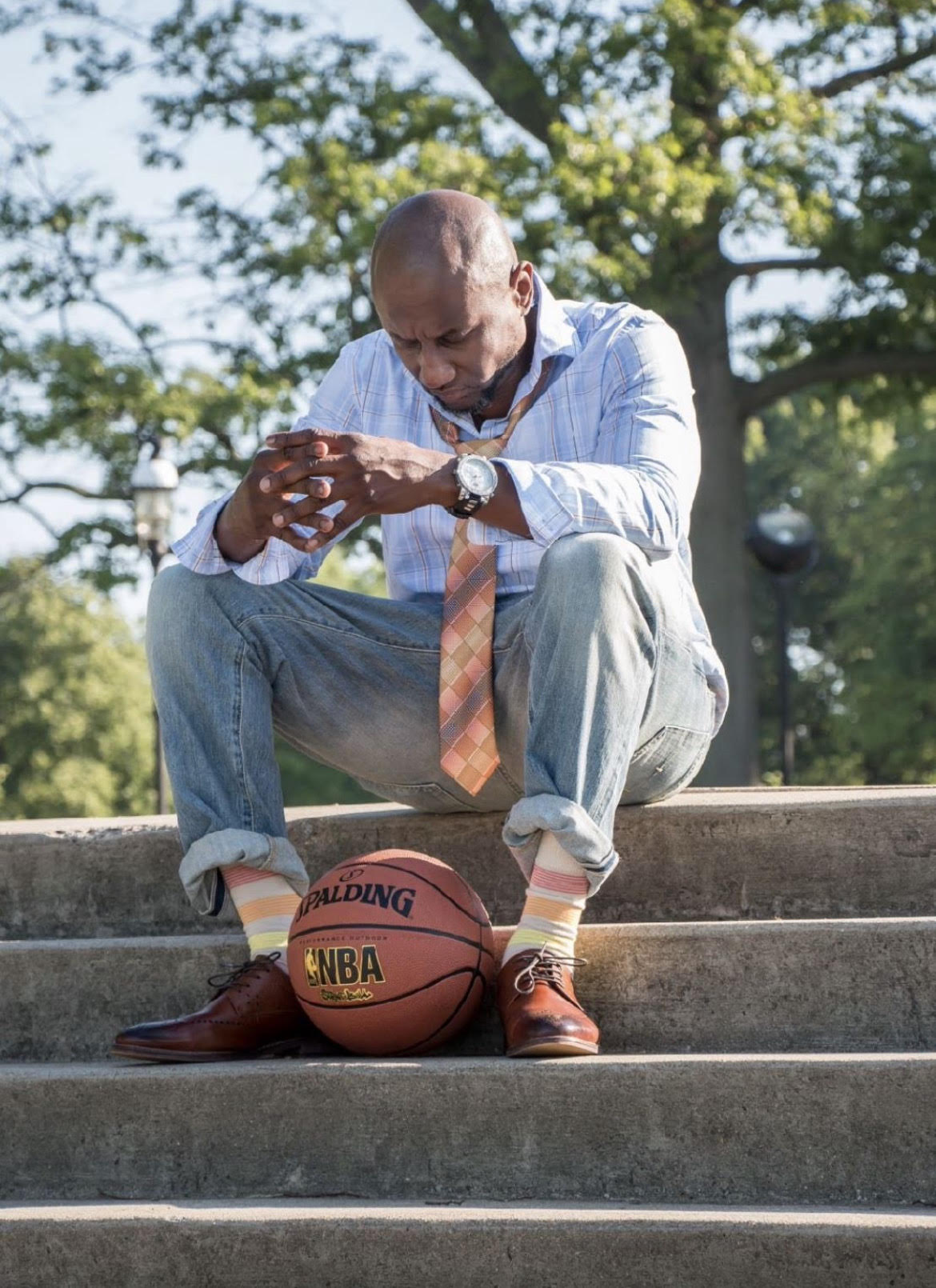 Photo of Taylor Paul seated on stairs, looking down, with a basketball at his feet