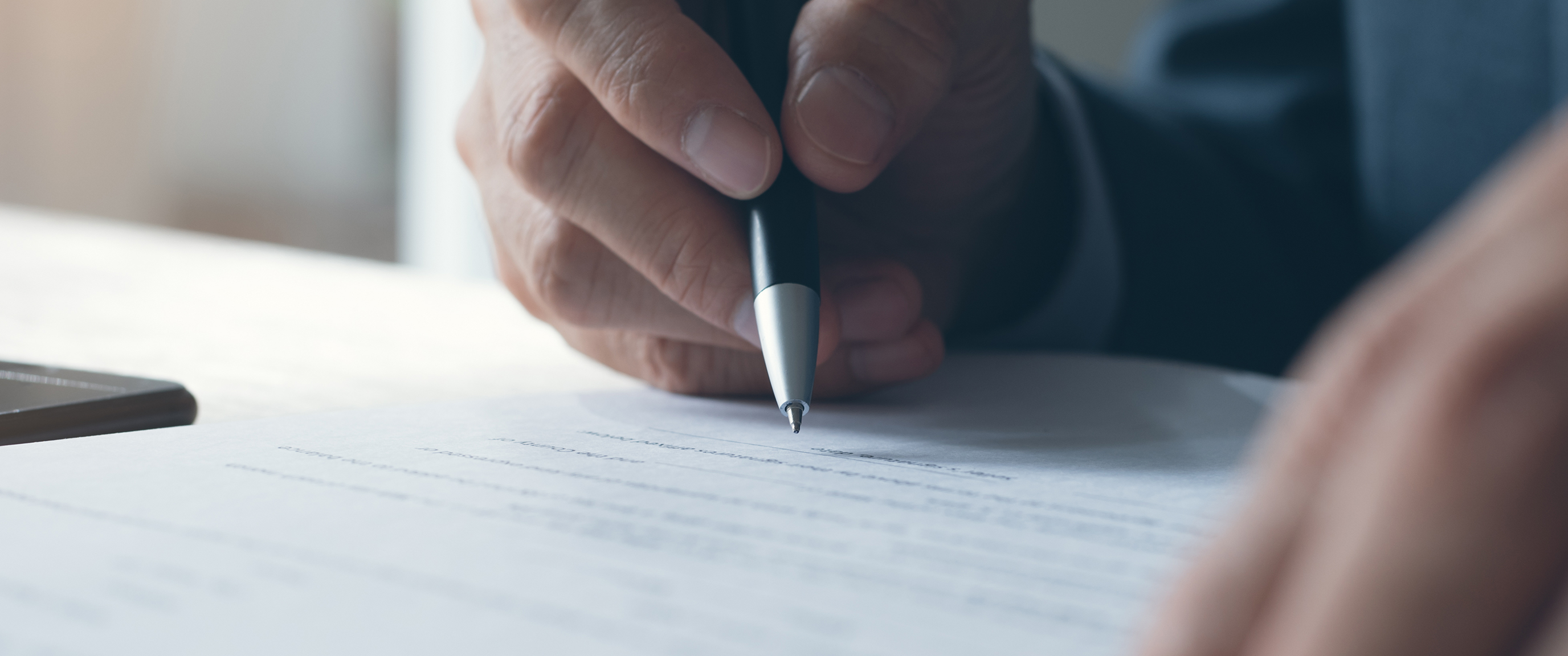 Hand signing a document with a pen.