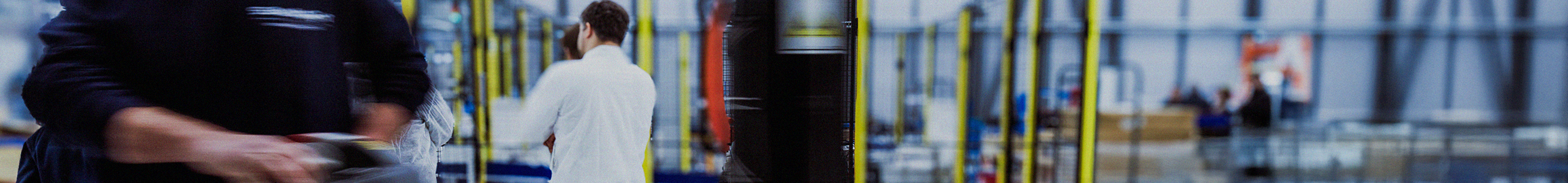 Workers moving through a factory floor with equipment in motion.