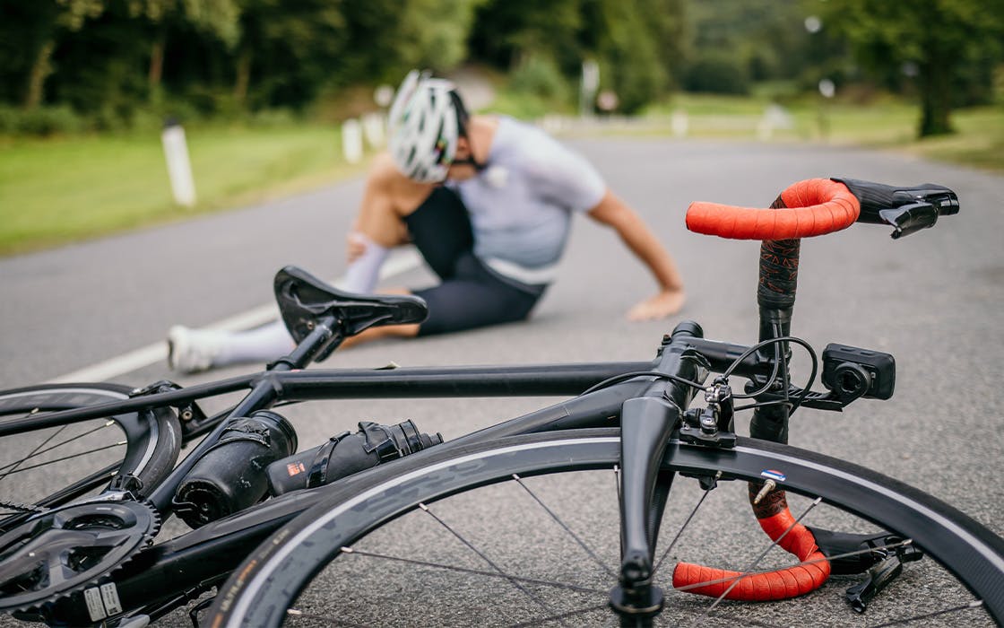 Bicycle laying on the ground and rider holding their legs