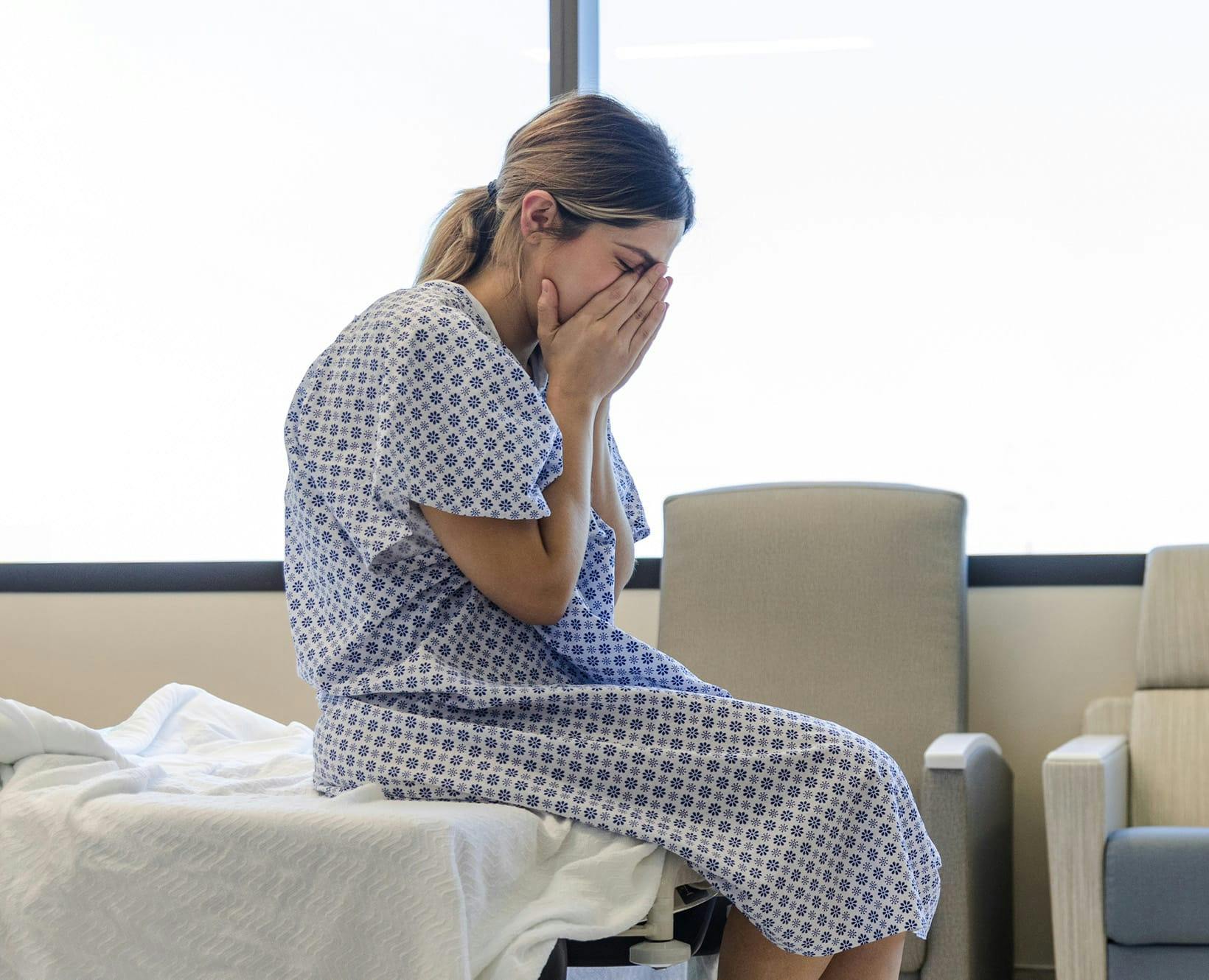 A woman in a hospital gown covering her face