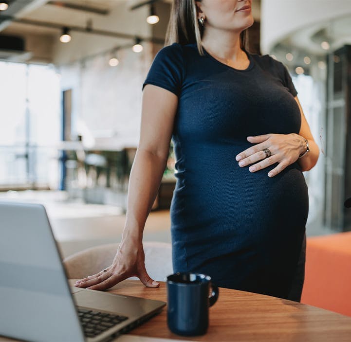 pregnant woman stinding next to a table with a laptop