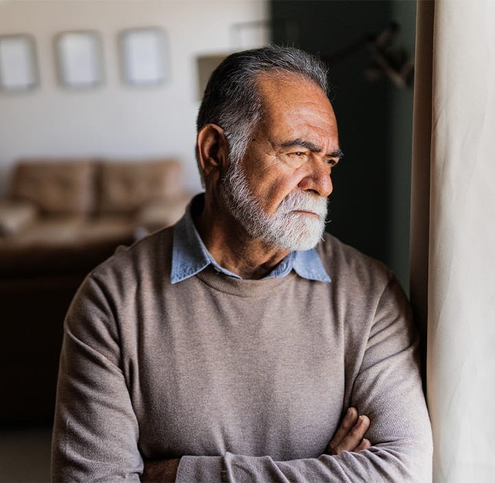 older man crossing his arms, looking out a window