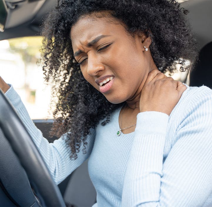 woman in a car, holding her neck in pain