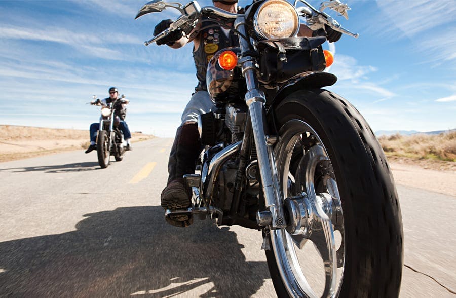 two people on motor cycles driving on a road in the desert