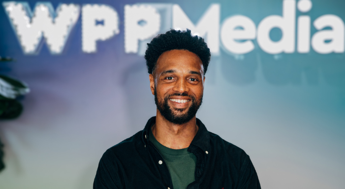 Portrait d'une personne debout devant un fond flou avec le logo "WPP Media" visible en arrière-plan.