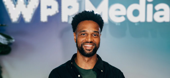 Portrait d'une personne debout devant un fond flou avec le logo "WPP Media" visible en arrière-plan.