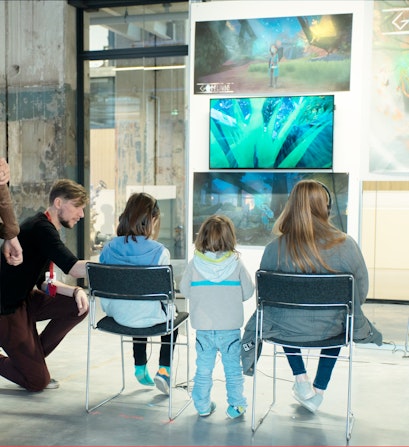 Een foto van mensen die op een stoel zitten en naar een expositie kijken