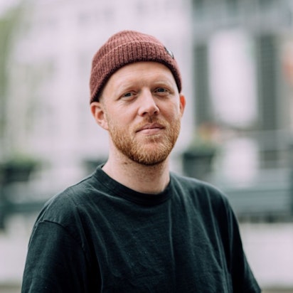 Portret van Nanne Wytze Brouwer. Hij draagt een zwart t-shirt en een bruine muts. De achtergrond is vervaagd.