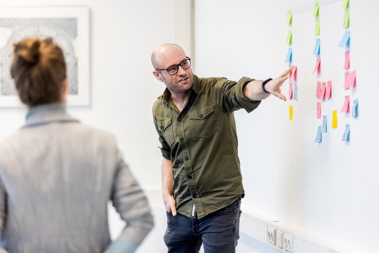 Alain wijst naar post-its op de muur.