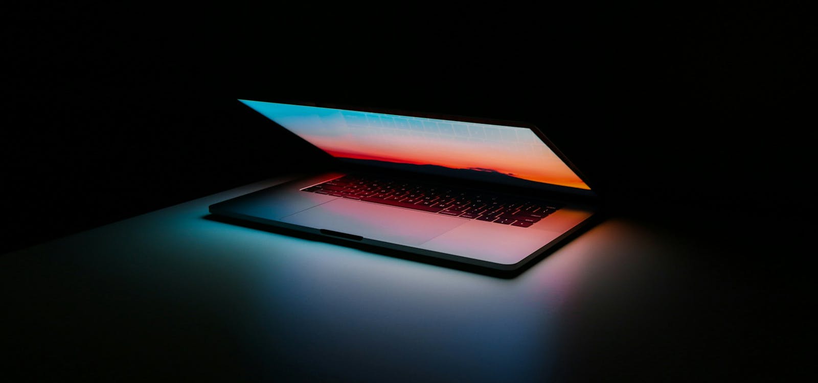 asdf A laptop with an illuminated keyboard and screen glowing in a dark room.