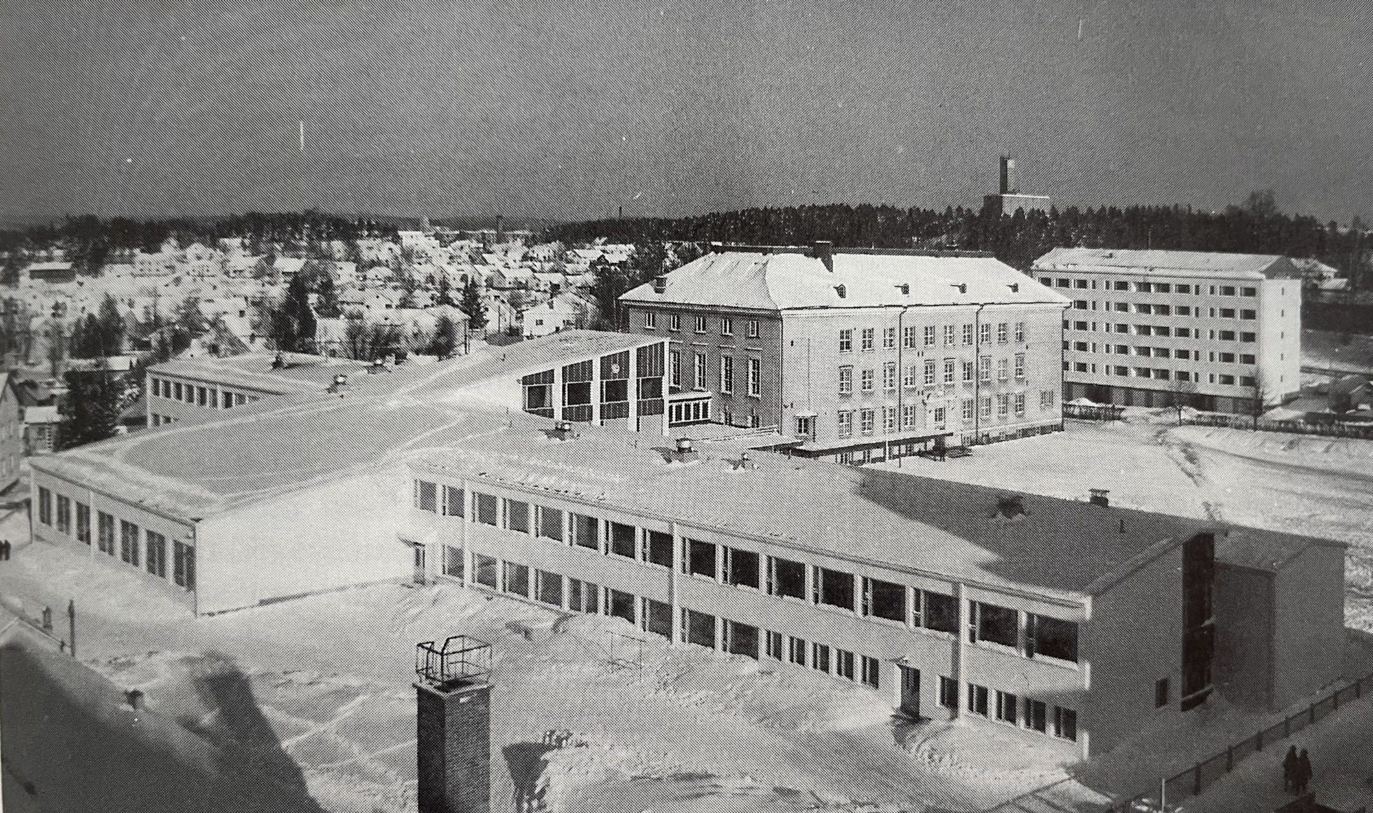 Kuvan etualalla on pitkän mallinen, kaksikerroksinen rakennus. Katolla ja maassa on lunta. Taustalla näkyy vanha Cygnaeuksen koulurakennus sekä lähiseudun rakennuksia