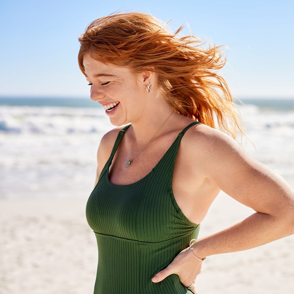 woman in green bathing suit smiling on the beach