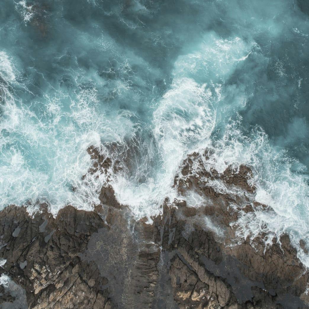 birds eye view of waves hitting rocky cliff
