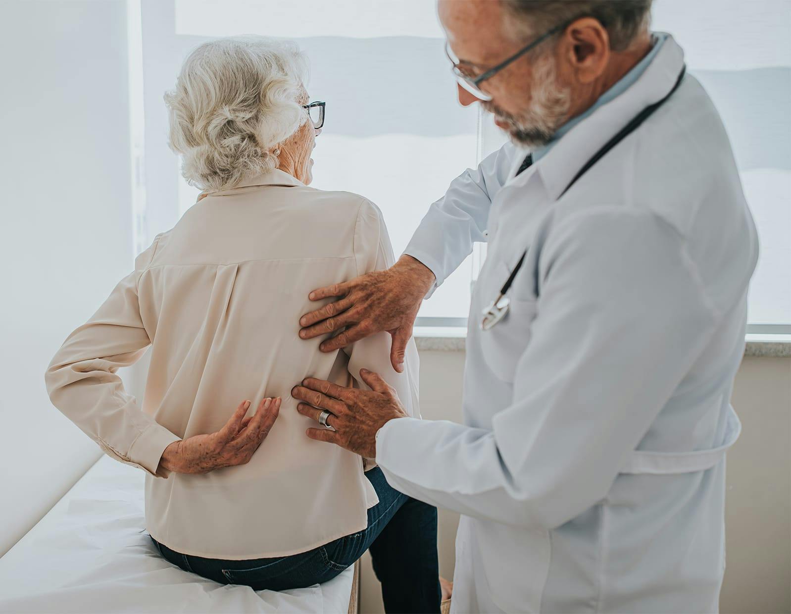 Doctor examining elderly woman’s lower back during check-up