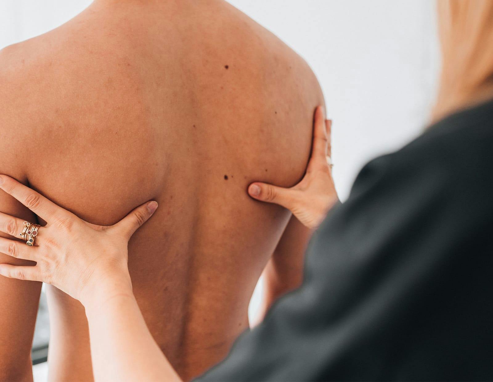 Healthcare provider assessing a patient's upper back and shoulder alignment with hands-on examination