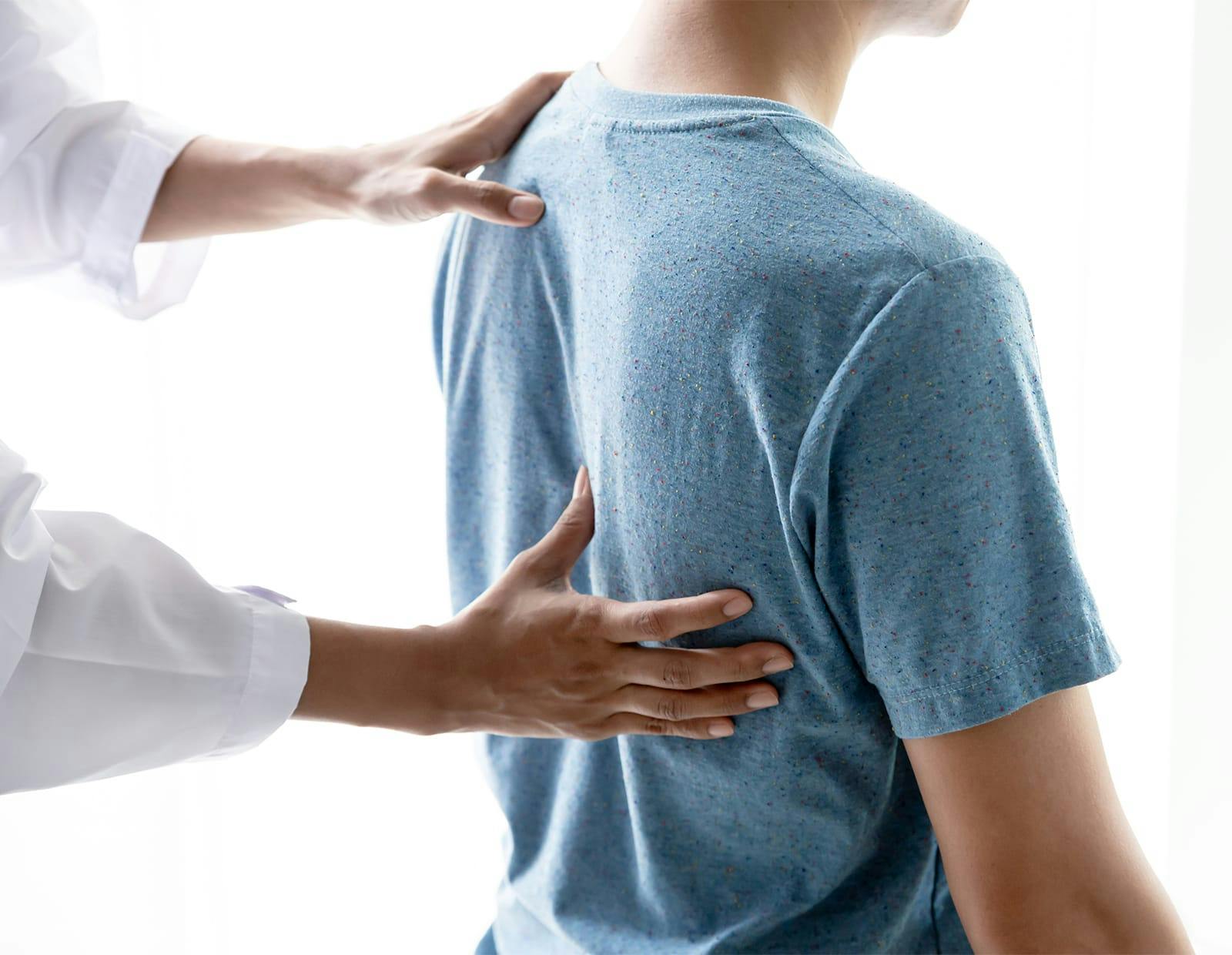 Medical practitioner assessing the upper back of a patient wearing a blue shirt