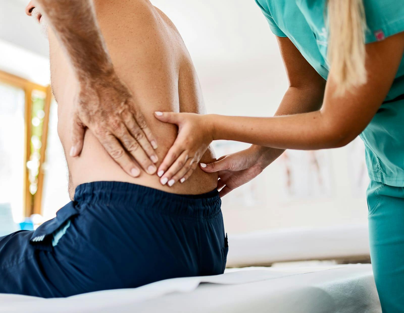Medical professional examining a patient's lower back while they're sitting