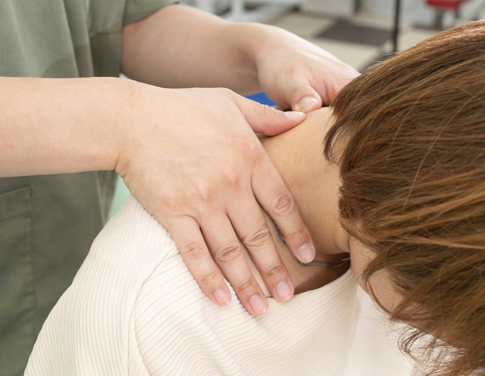 Medical professional palpating the neck and upper shoulder of a seated patient
