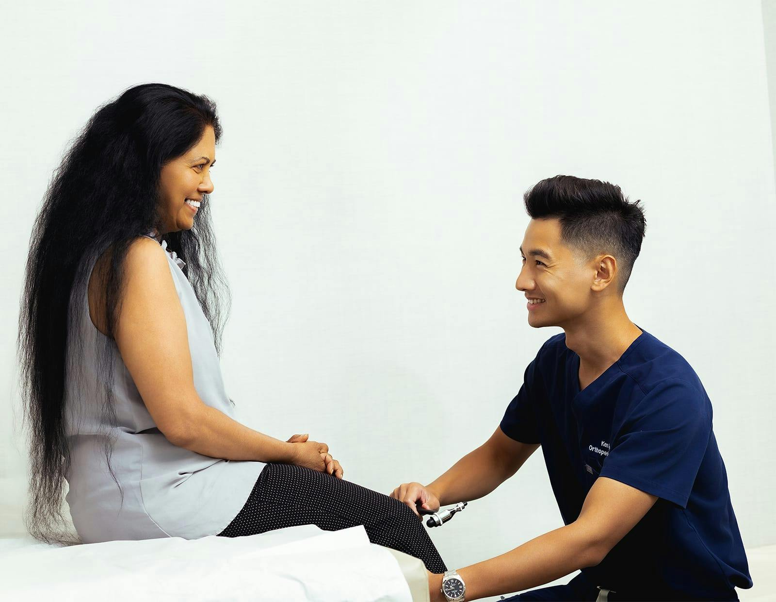 Healthcare provider in navy scrubs using a reflex hammer to assess a patient's knee response during a physical exam