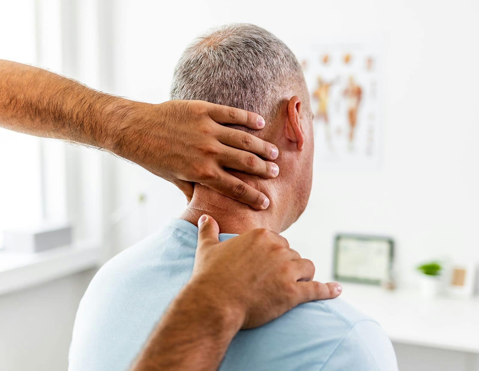 Healthcare provider examining the neck and upper spine of an older male patient during a physical assessment