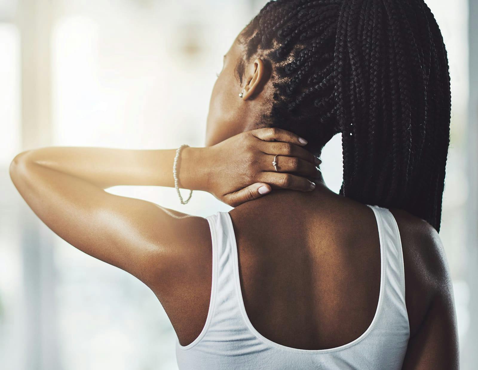 Young woman experiencing neck pain, reaching back to touch the base of her neck
