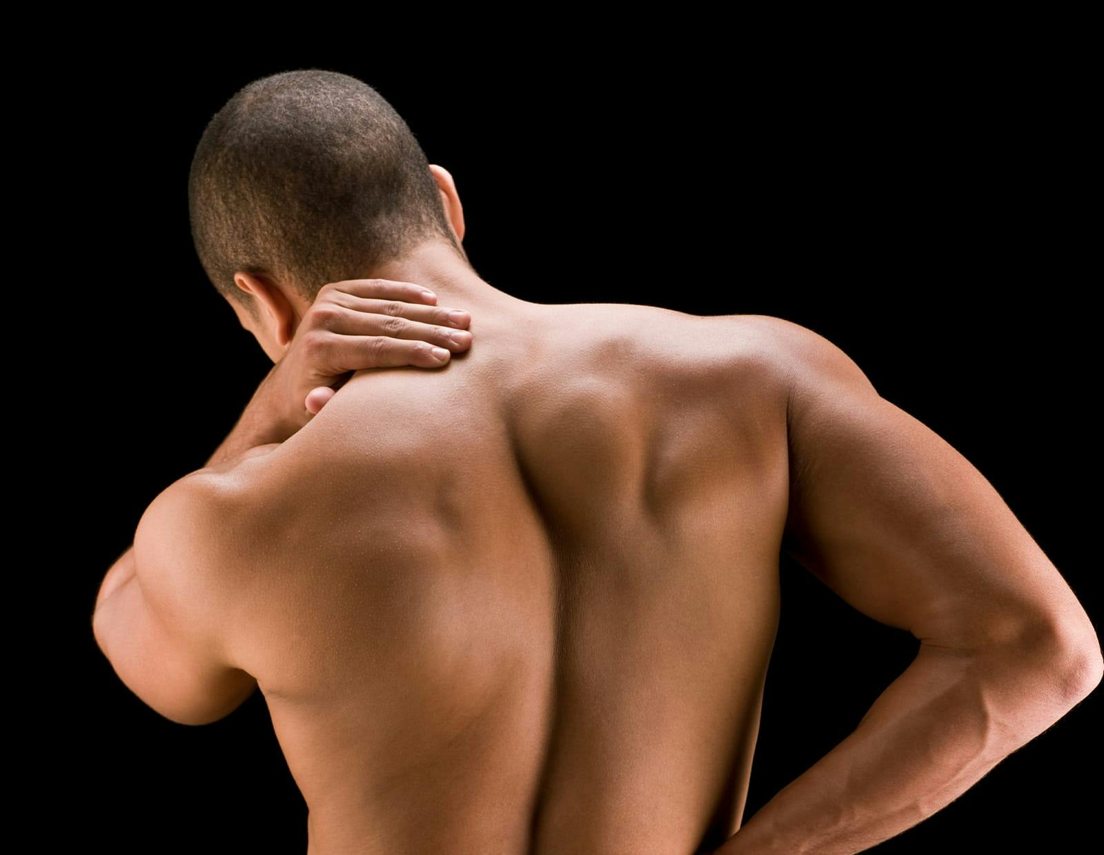 Man with muscular build holding his neck and upper back in discomfort, indicating spine or muscle pain