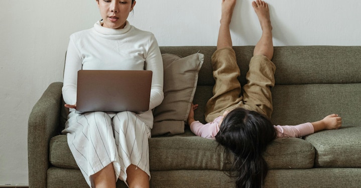 Parent typing on laptop with kid upside down on couch