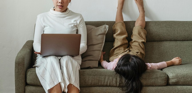 Parent typing on laptop with kid upside down on couch