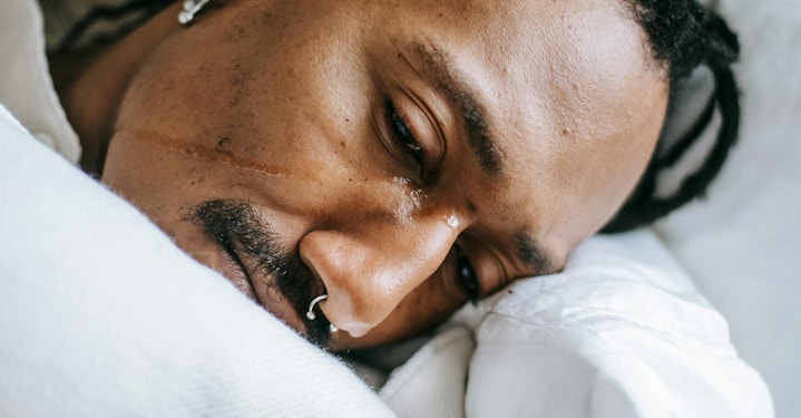 Person lying in bed with a tear on cheek, showing signs of persistent sadness or emotional distress