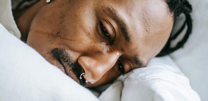 Person lying in bed with a tear on cheek, showing signs of persistent sadness or emotional distress