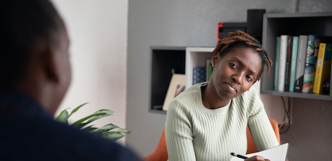 Therapist writing down notes and looking intently at other person
