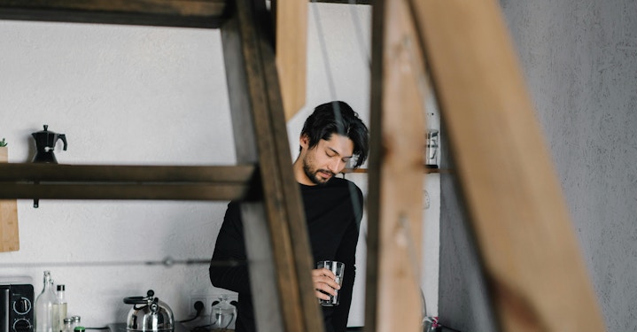 A person stands in a kitchen, staring at a glass of water, hinting at his inner battle with high functioning depression