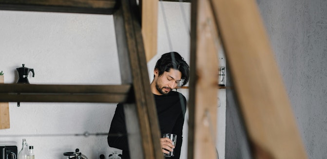 A person stands in a kitchen, staring at a glass of water, hinting at his inner battle with high functioning depression
