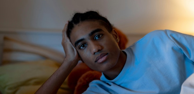 A young person lying in bed with their head on a pillow, propping up their head and appearing deep in thought, suggesting possible signs of depression.