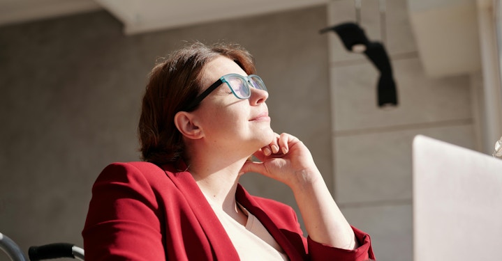 A person wearing glasses sits calmly at a table with a laptop