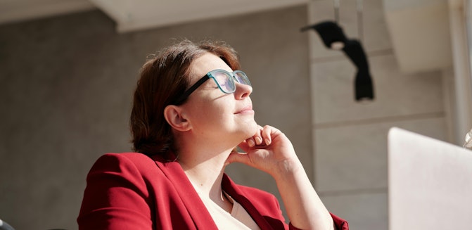 A person wearing glasses sits calmly at a table with a laptop