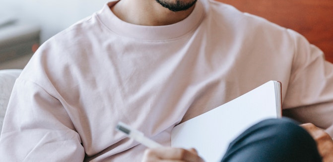 person journaling for mental health, holding notebook on their lap while writing