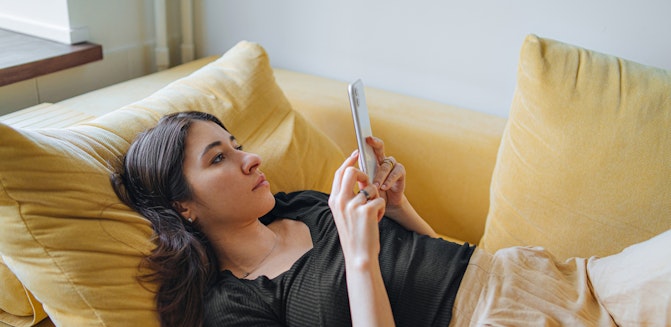 A person lying on a couch, browsing their phone to learn about therapy expenses