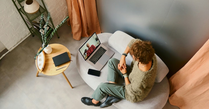 A person sitting on a couch with hands crossed, talking to their therapist on a video call about ending therapy.